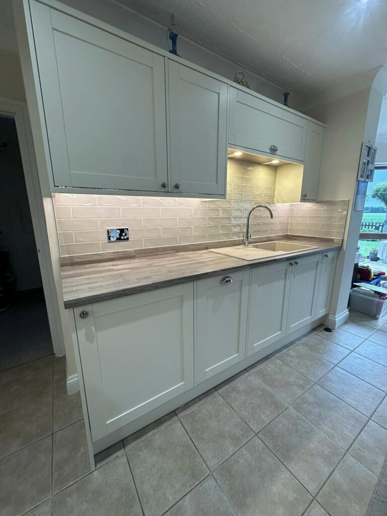 Modern kitchen units with white cupboard doors and grey wooden countertops. A sink is visible.