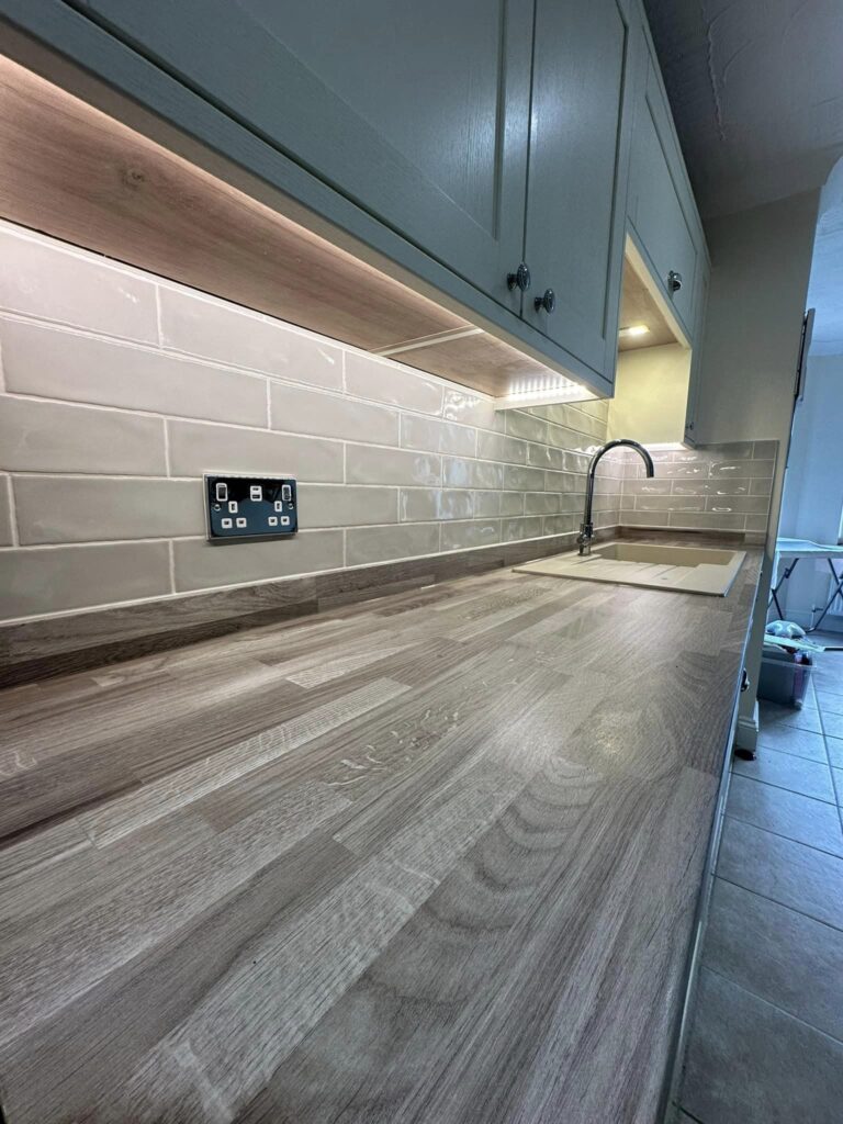 A close up along the counter of modern kitchen units with white cupboard doors and grey wooden countertops. A sink is visible.