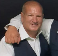 A man in a waistcoat smiling at the camera with the arm of another man around his neck